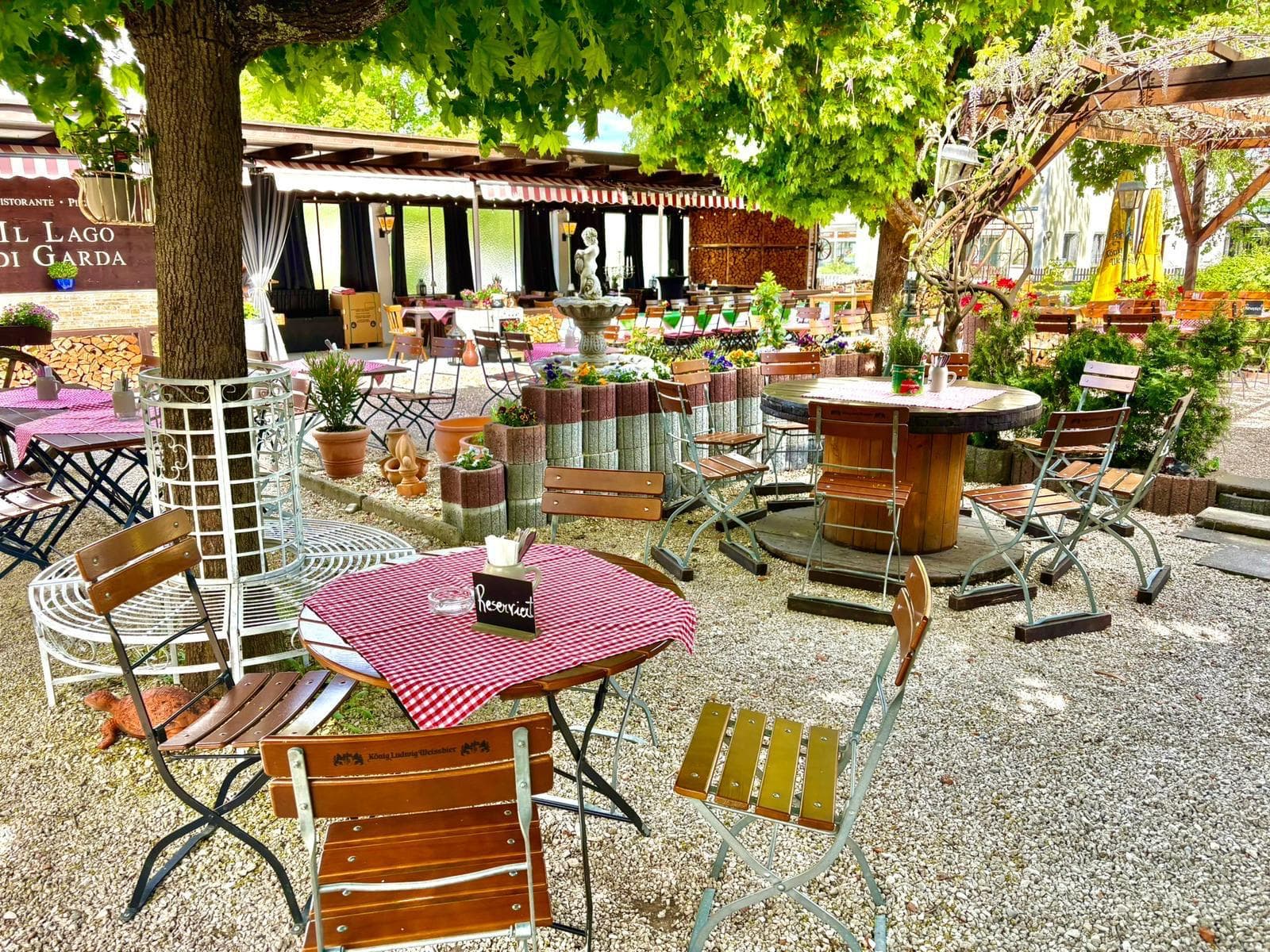 Biergartentische mit rot-weiß karierten Decken im Schatten eines alten Baums